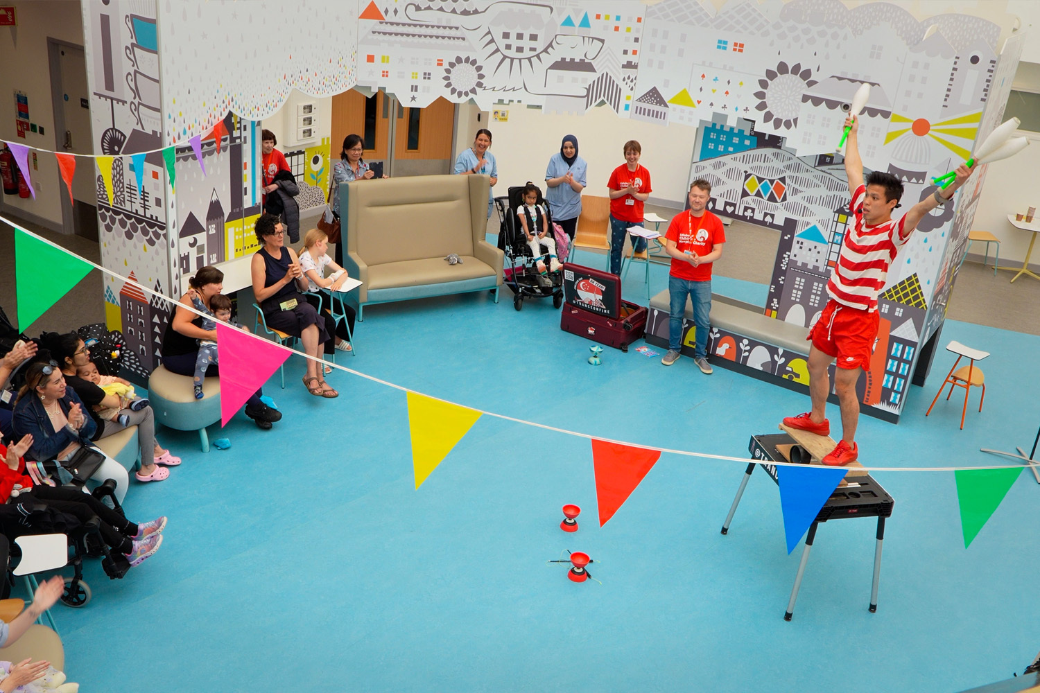 A Fringe performer balances on a table while holding juggling clubs aloft during a performance at the Edinburgh Children's Hospital.