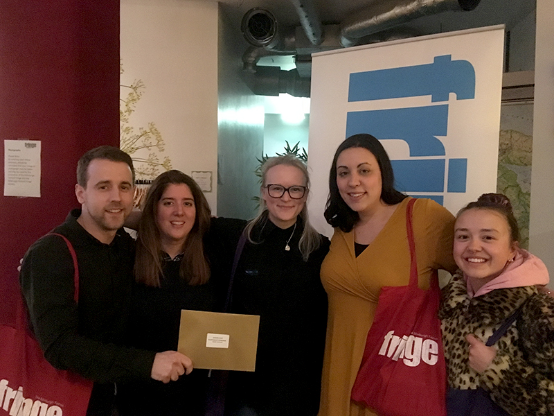 A group of five people holding a gold envelope to celebrate winning the quiz